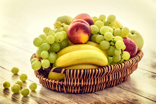 Cos din rachita plin cu struguri, banane, nectarine si mere verzi