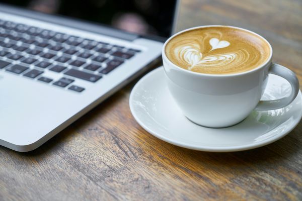 Laptop argintiu deschis pe o masa rustica din lemn, langa o cana de cafea